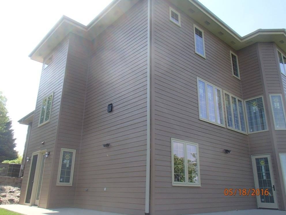 Tan house exterior with multiple windows and light-colored trim, set against a sunny sky.