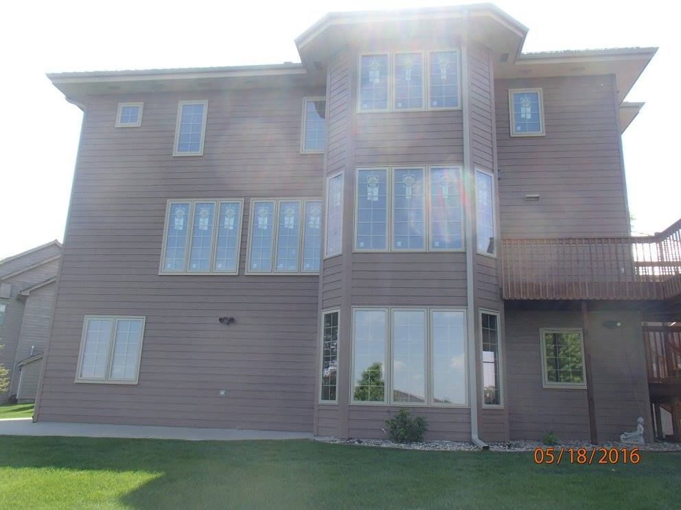 Back view of a two-story brown house with multiple windows; some windows are covered, green lawn in foreground.