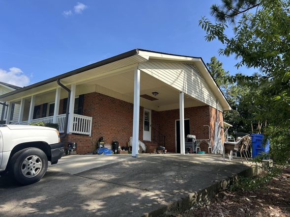 A brick house with a covered carport, white pillars, and a white pickup truck parked in front.