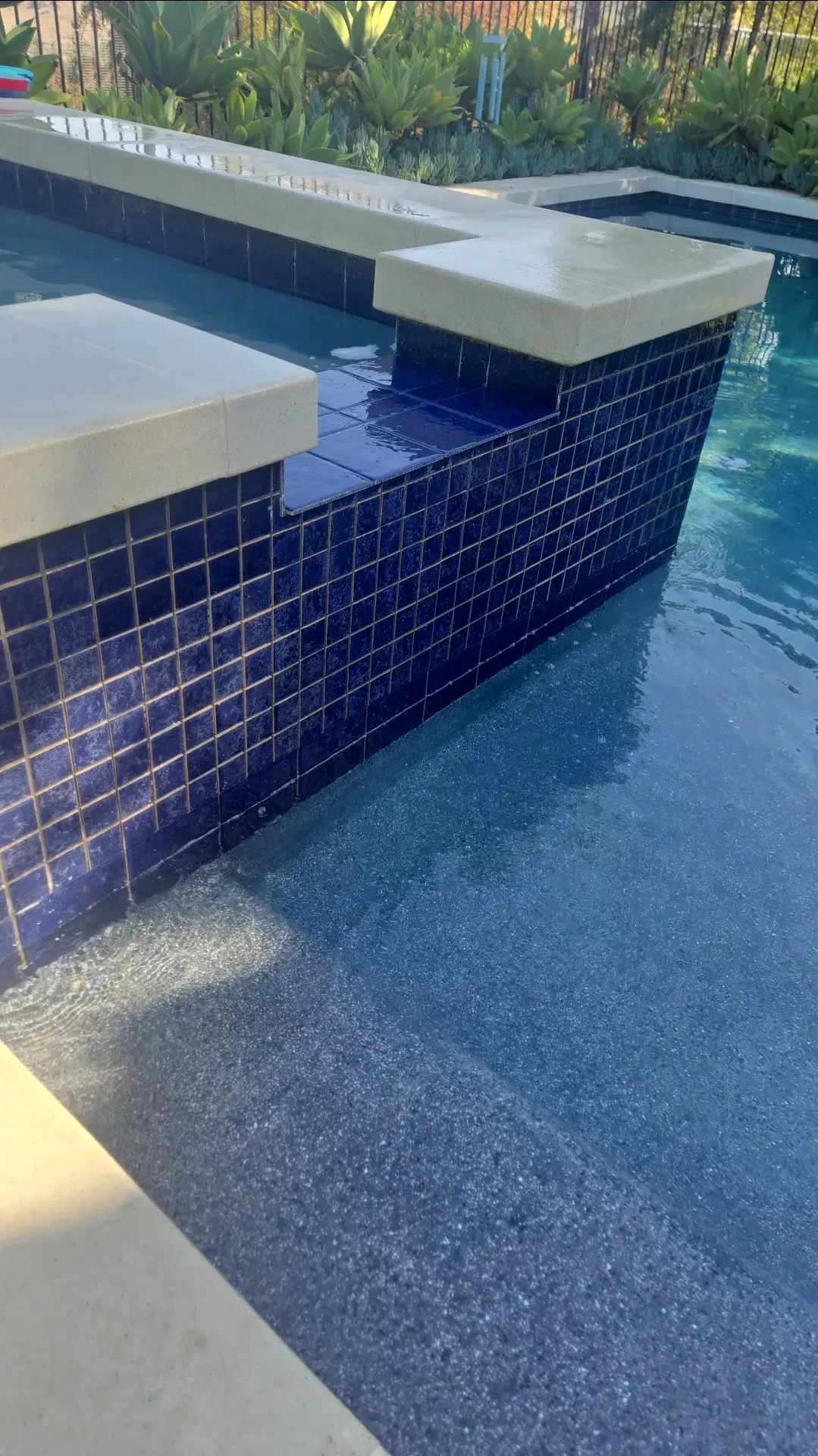 Blue tiled pool with concrete coping, partially filled with water, outdoor setting.