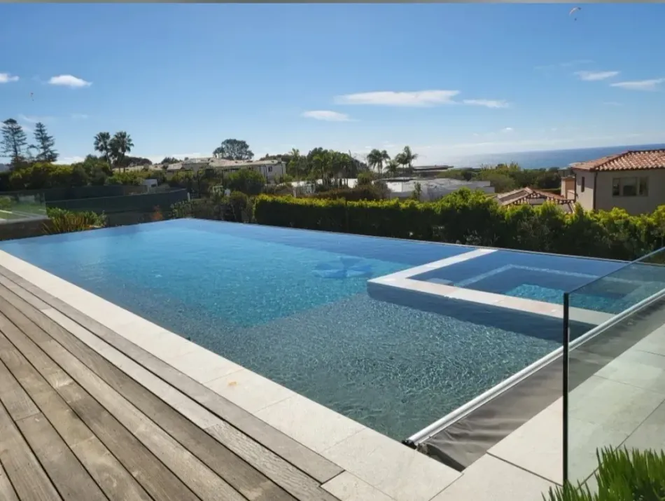 Swimming pool and jacuzzi with a view of homes and the ocean on a sunny day.