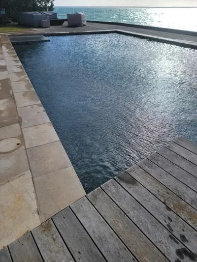 Pool with wooden deck and stone surround, overlooking the ocean on a sunny day.