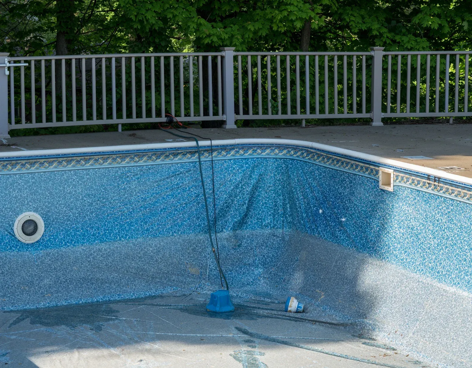 Swimming pool with jacuzzi, surrounded by concrete, grass, and trees, mountains in background.