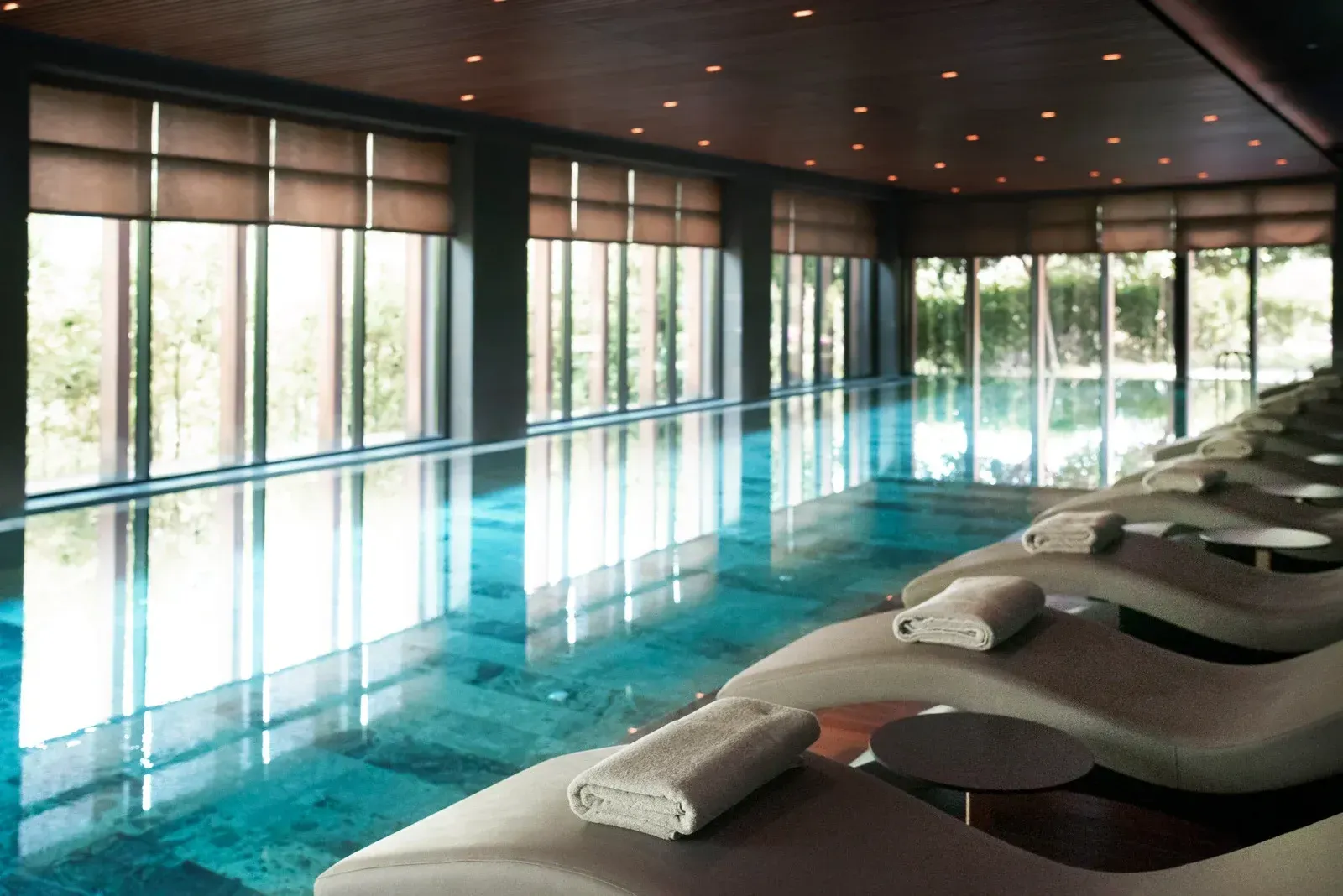 Indoor spa pool with lounge chairs, large windows, and ambient lighting.