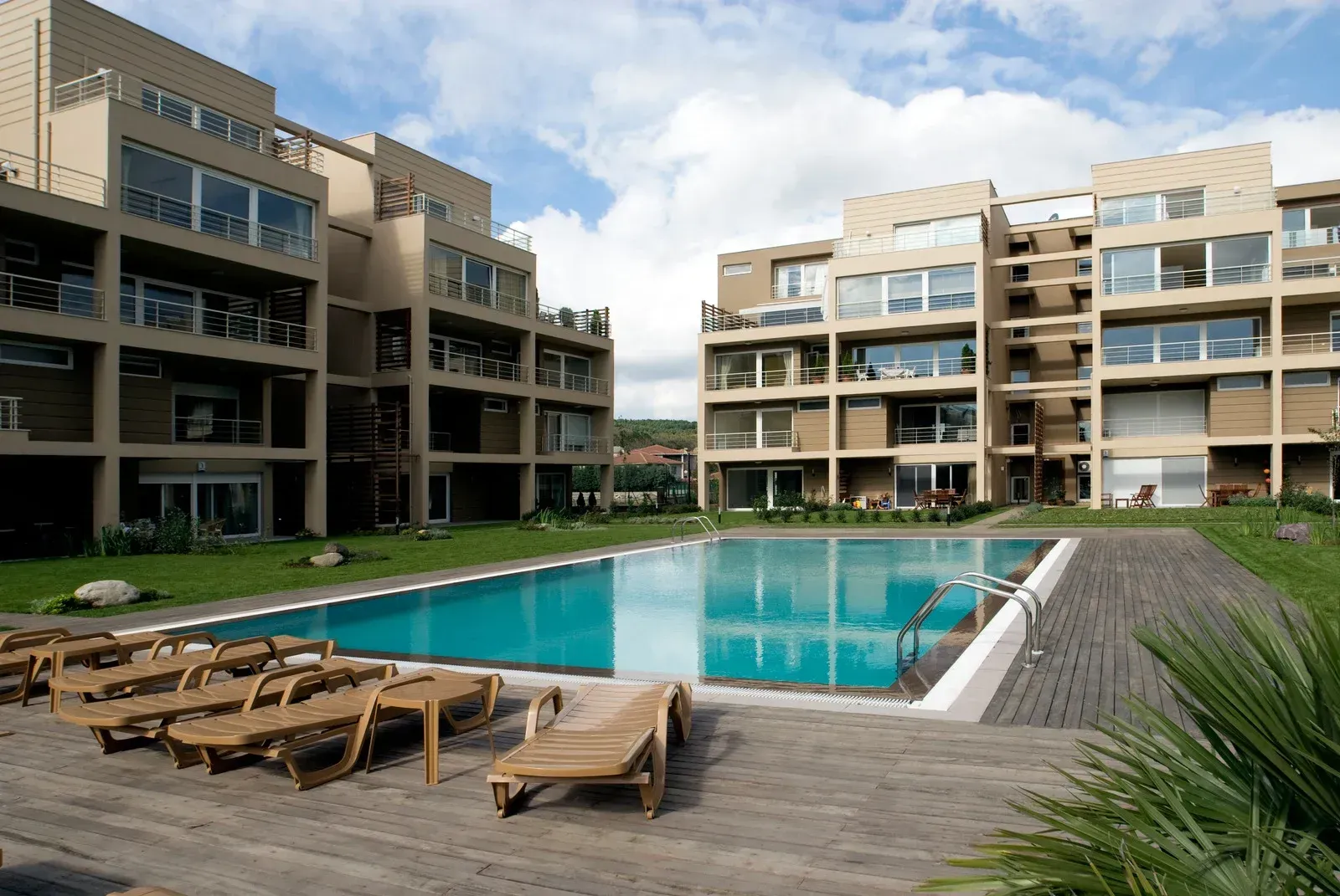 Apartment buildings with a swimming pool and lounge chairs on a sunny day.