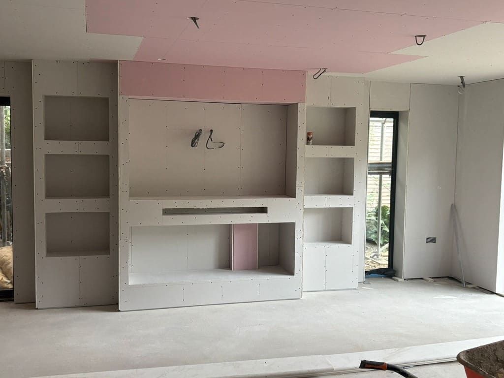 Interior construction: Metal studs form room framing; visible pink insulation, concrete floor. Red power tool, lights present.