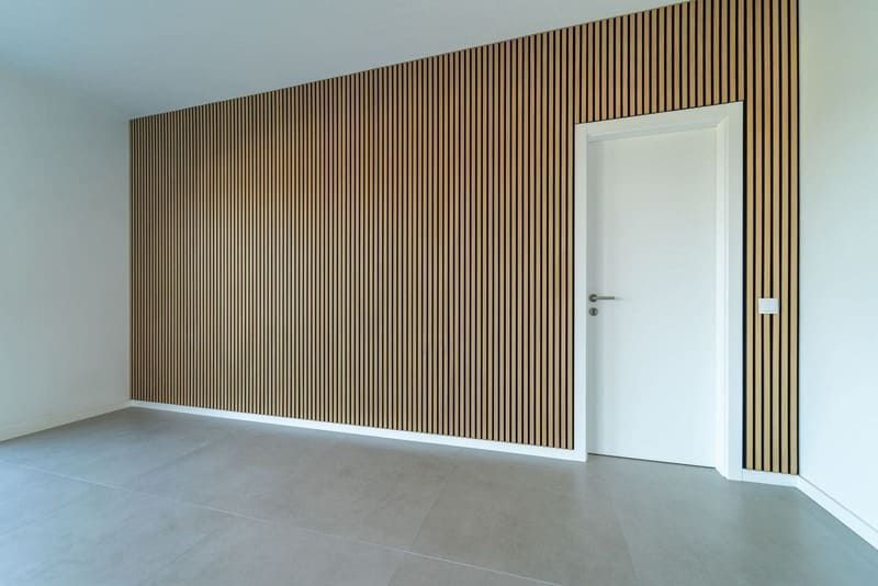 Empty room with a wooden slatted accent wall, white door, and gray floor.