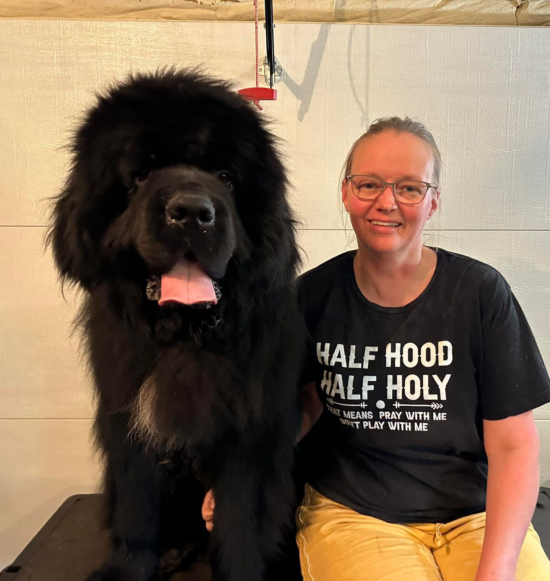 A woman is sitting next to a large black dog wearing a half hood half holy shirt