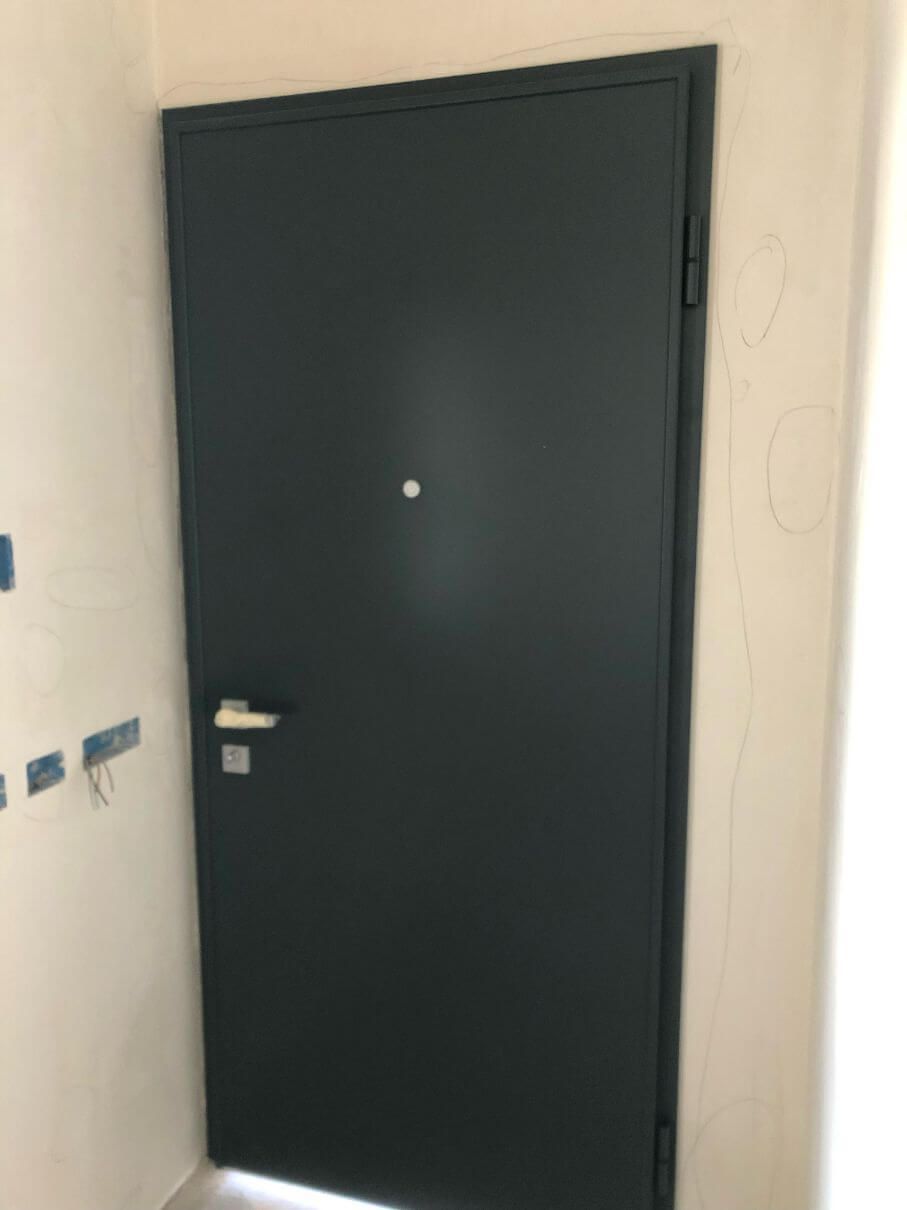 Una porta nera si trova in una stanza accanto a un muro bianco.