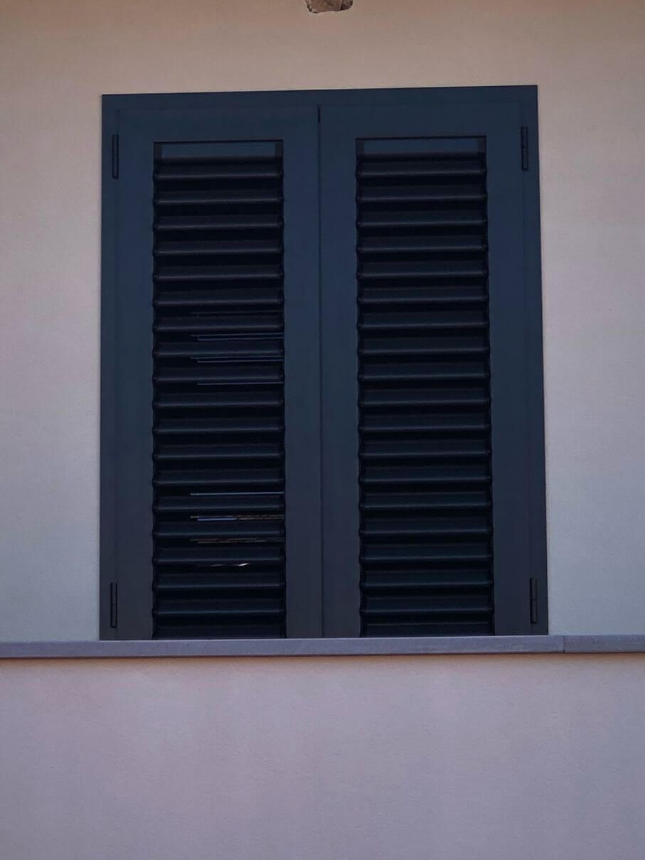 Una finestra con persiane nere su un muro bianco.