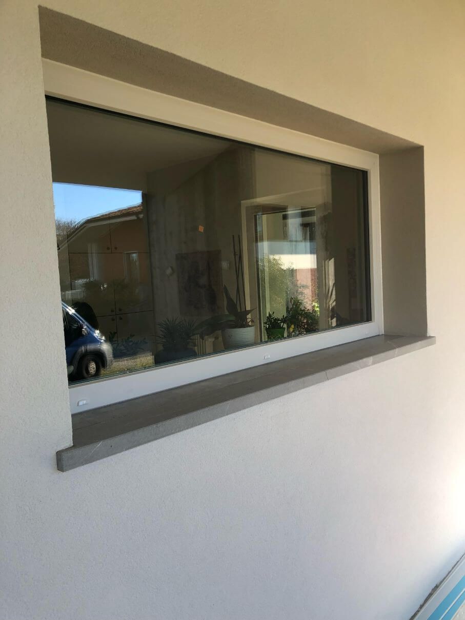 Una grande finestra su un muro bianco in cui è riflessa un'auto.