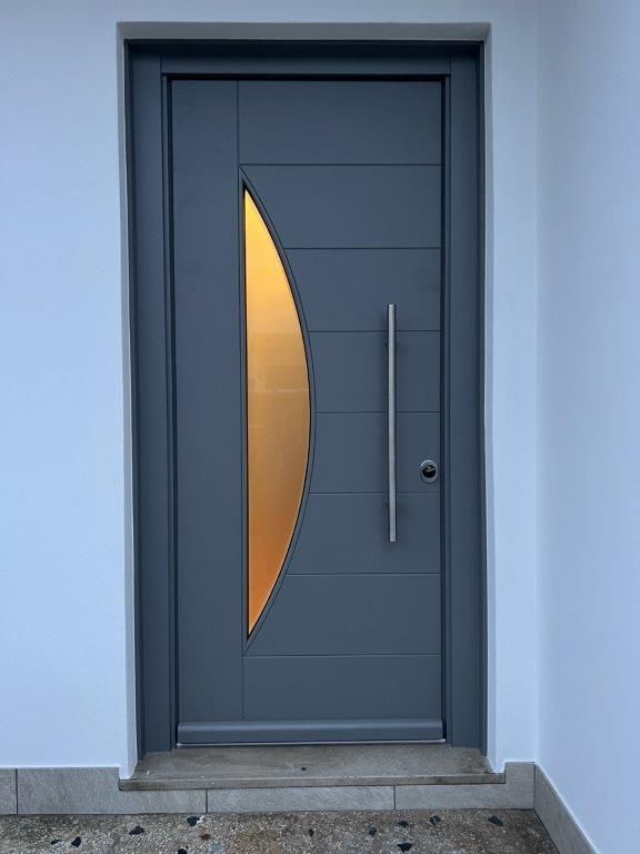 Una porta grigia con una maniglia in acciaio inossidabile e una finestra a mezzaluna.