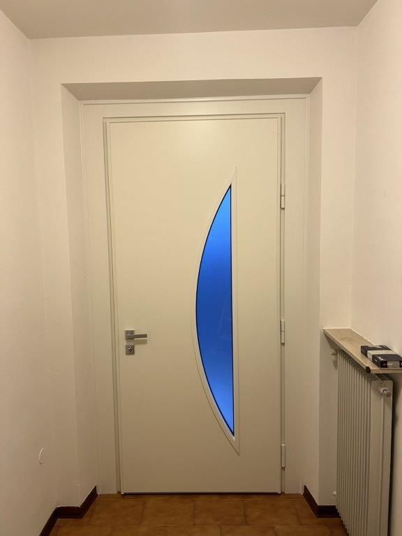 Una porta bianca con una finestra blu in un corridoio.