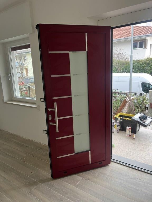 Una porta rossa è aperta in una stanza con una finestra.