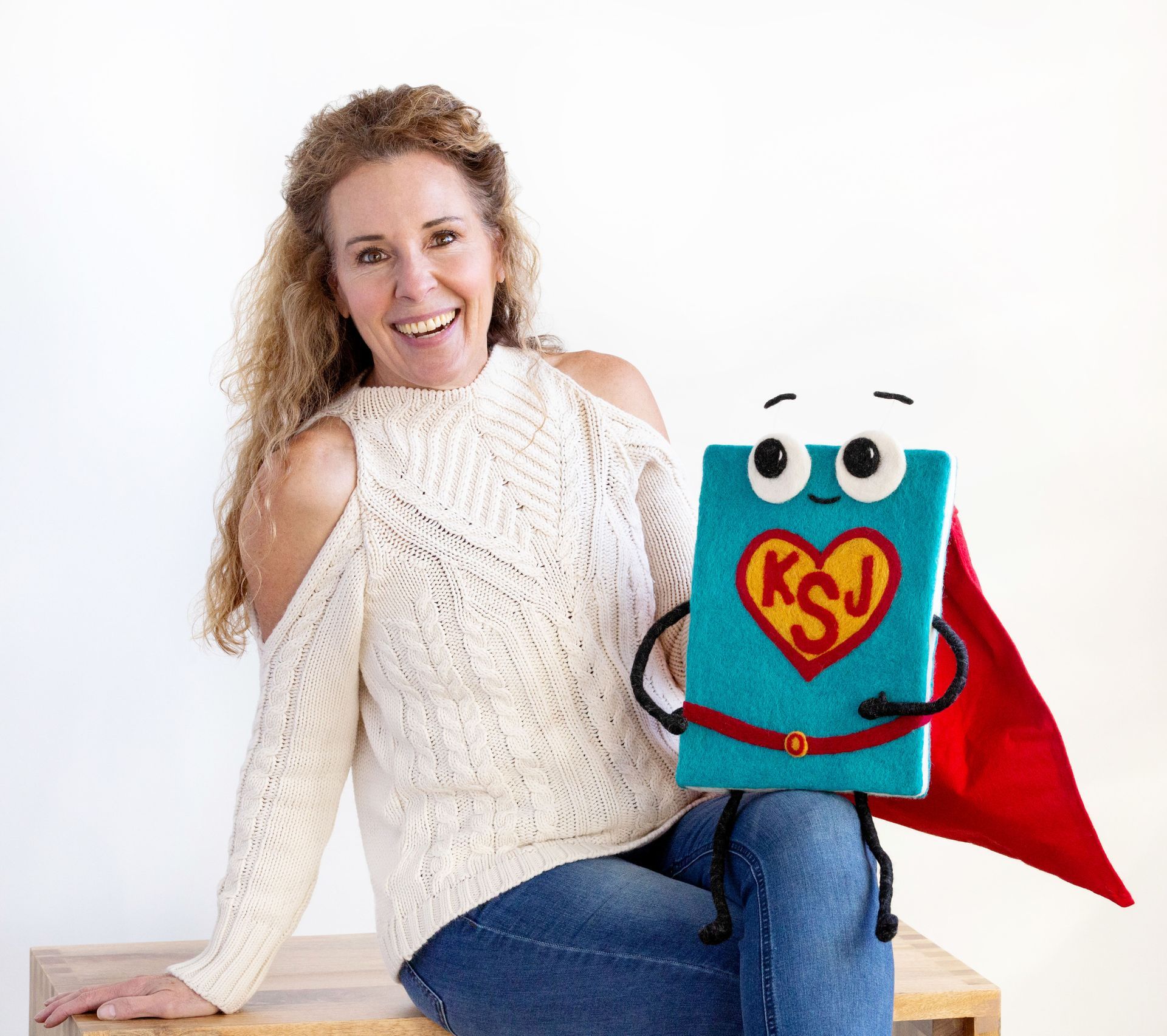 Woman with shoulder cut-outs sits beside a book character with a cape and heart, both smiling.