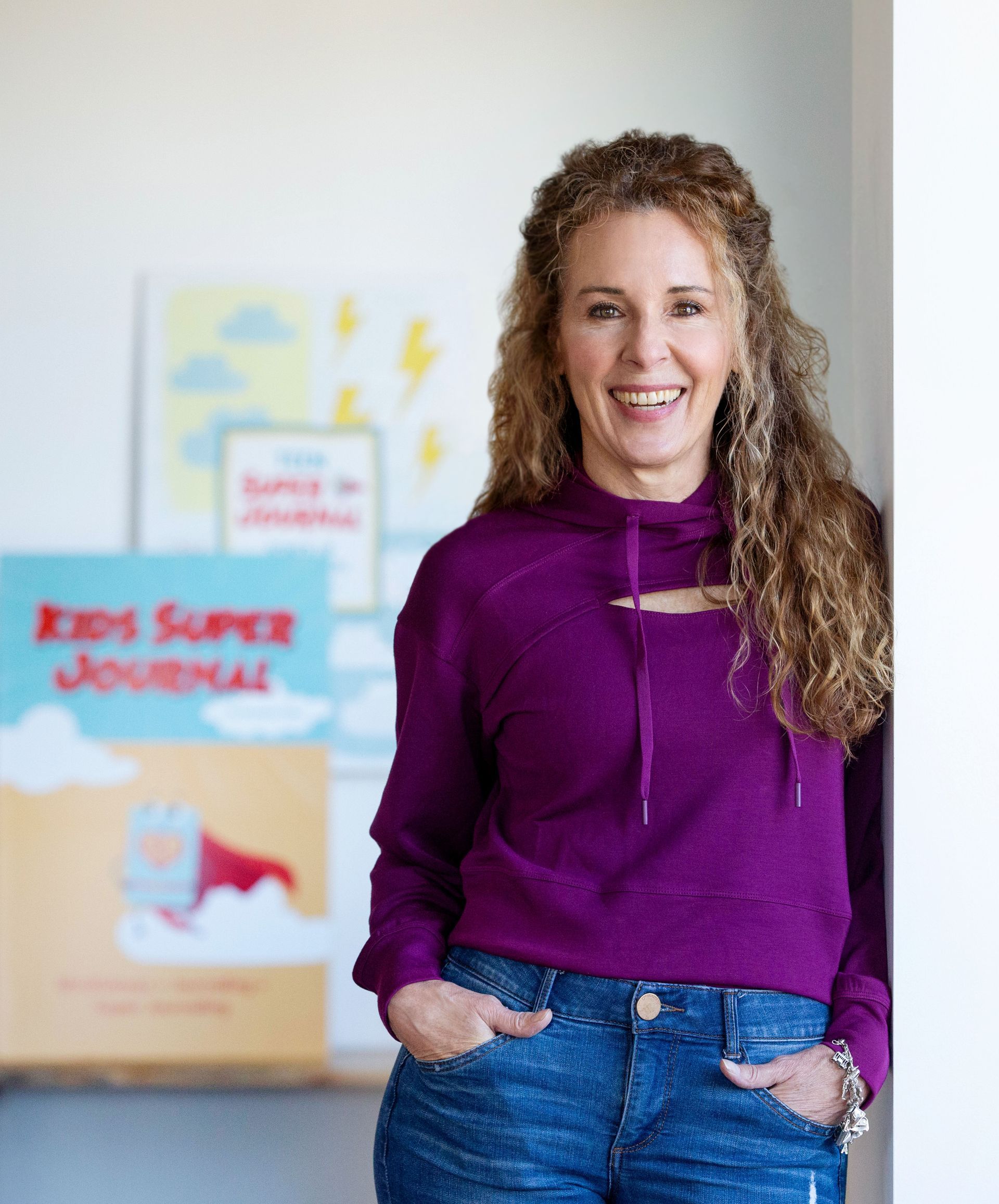 Woman with curly hair smiles, leans against a wall near children's book titled