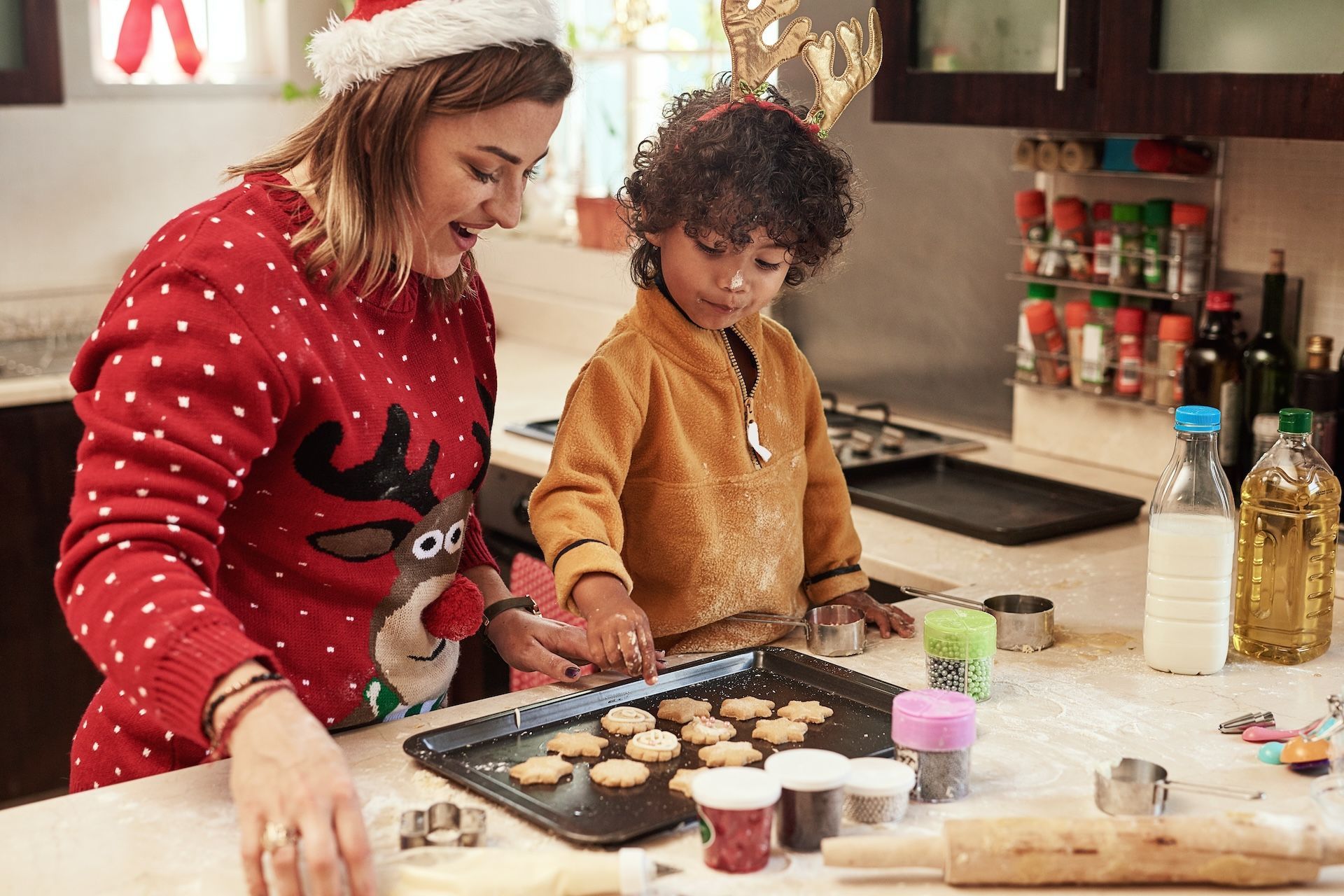 Montessori guide in Santa hat and child baking cookies in a kitchen, decorating with sprinkles and cutouts.
