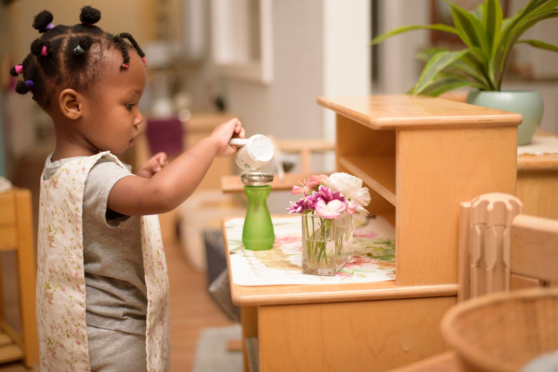 Montessori child pouring from a container into a green bottle, inside a well-lit room.