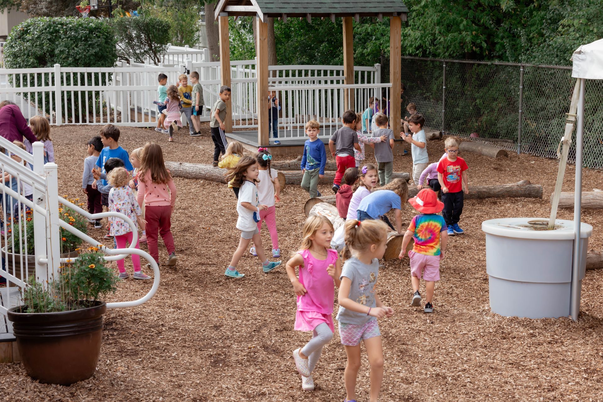 Montessori children playing in a wood-chipped playground near a small gazebo and white fence.