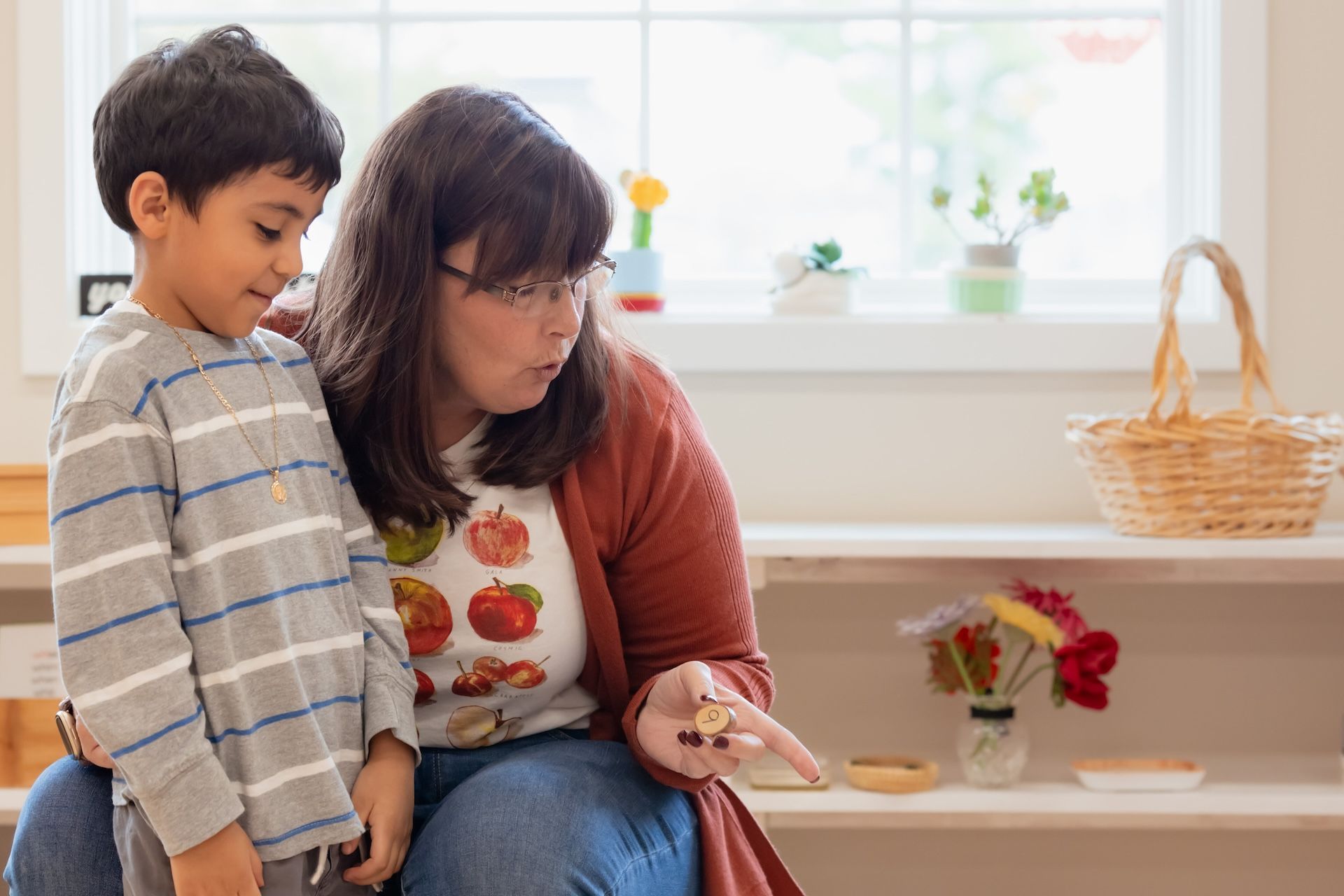 Montessori guide and a child looking at objects on a shelf in a bright room.