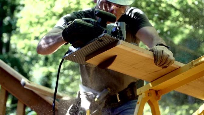 Carpenter cutting a wood plank with a circular saw.