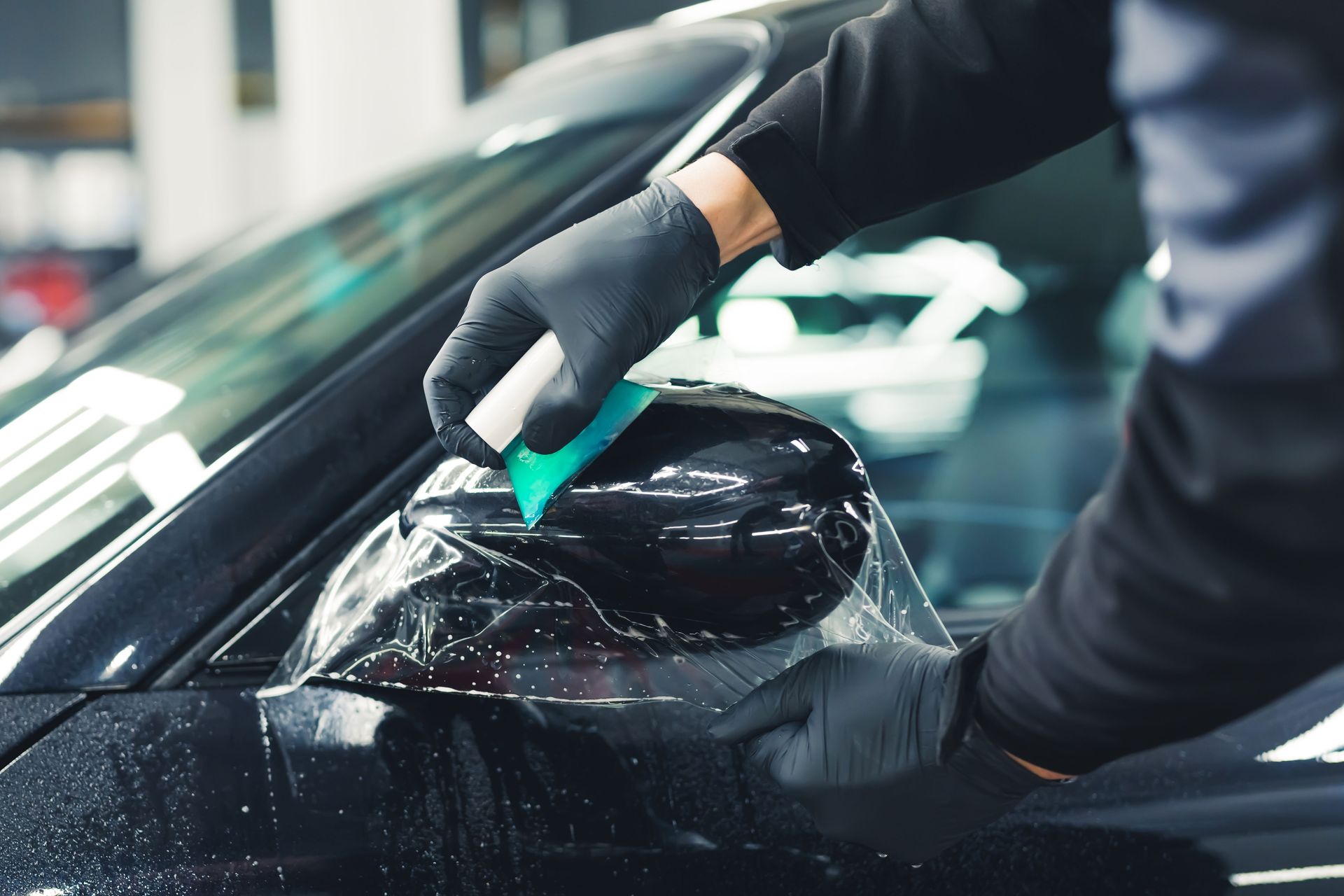 Person applying window film to a dark blue car in a workshop