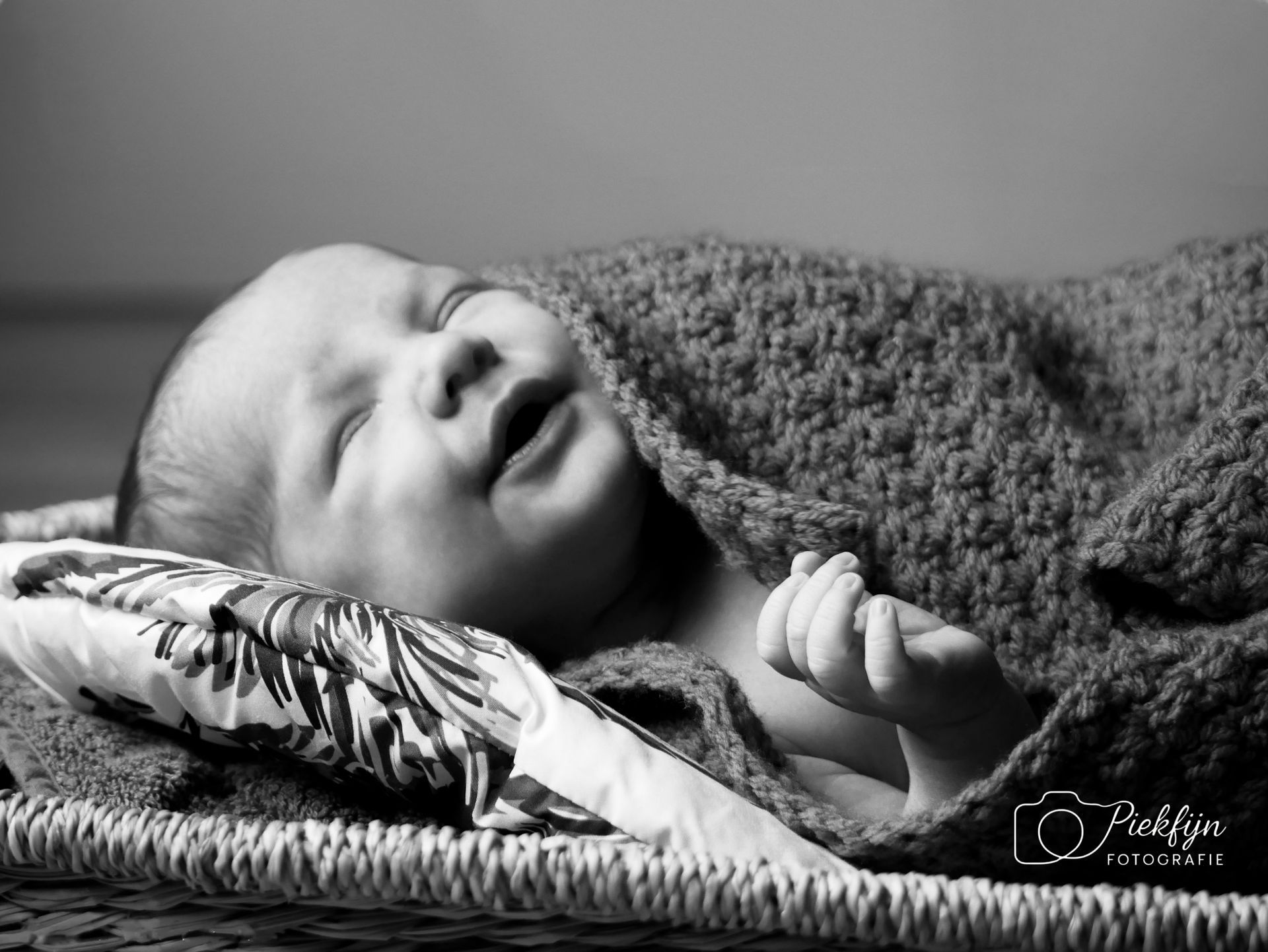 Een zwart-witfoto van een pasgeboren baby, gewikkeld in een deken.