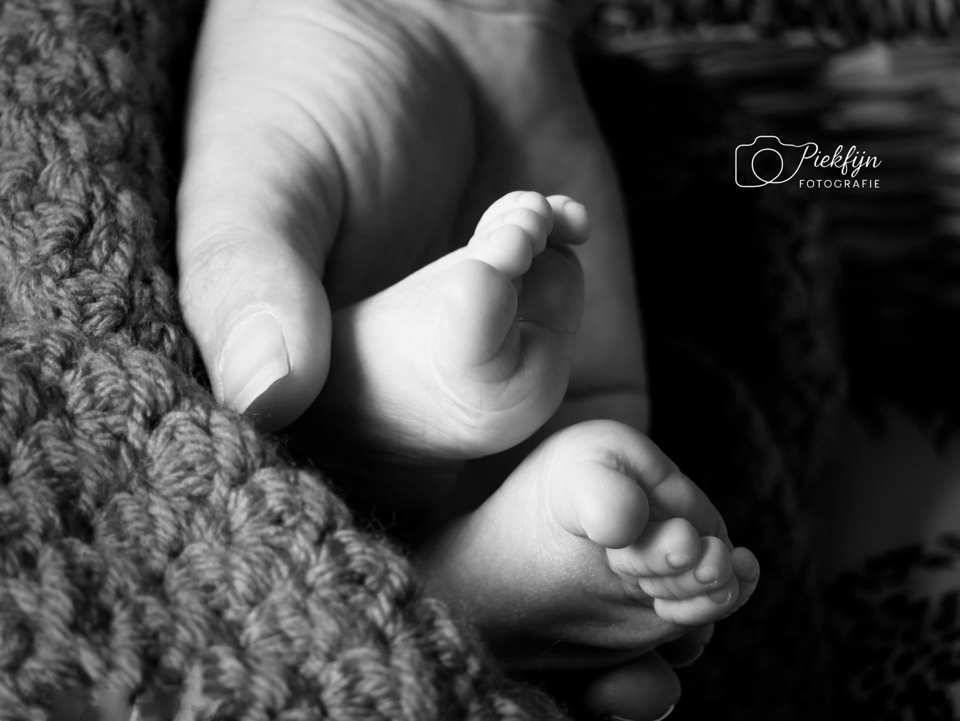 Een zwart-witfoto van een persoon die de voet van een baby vasthoudt.