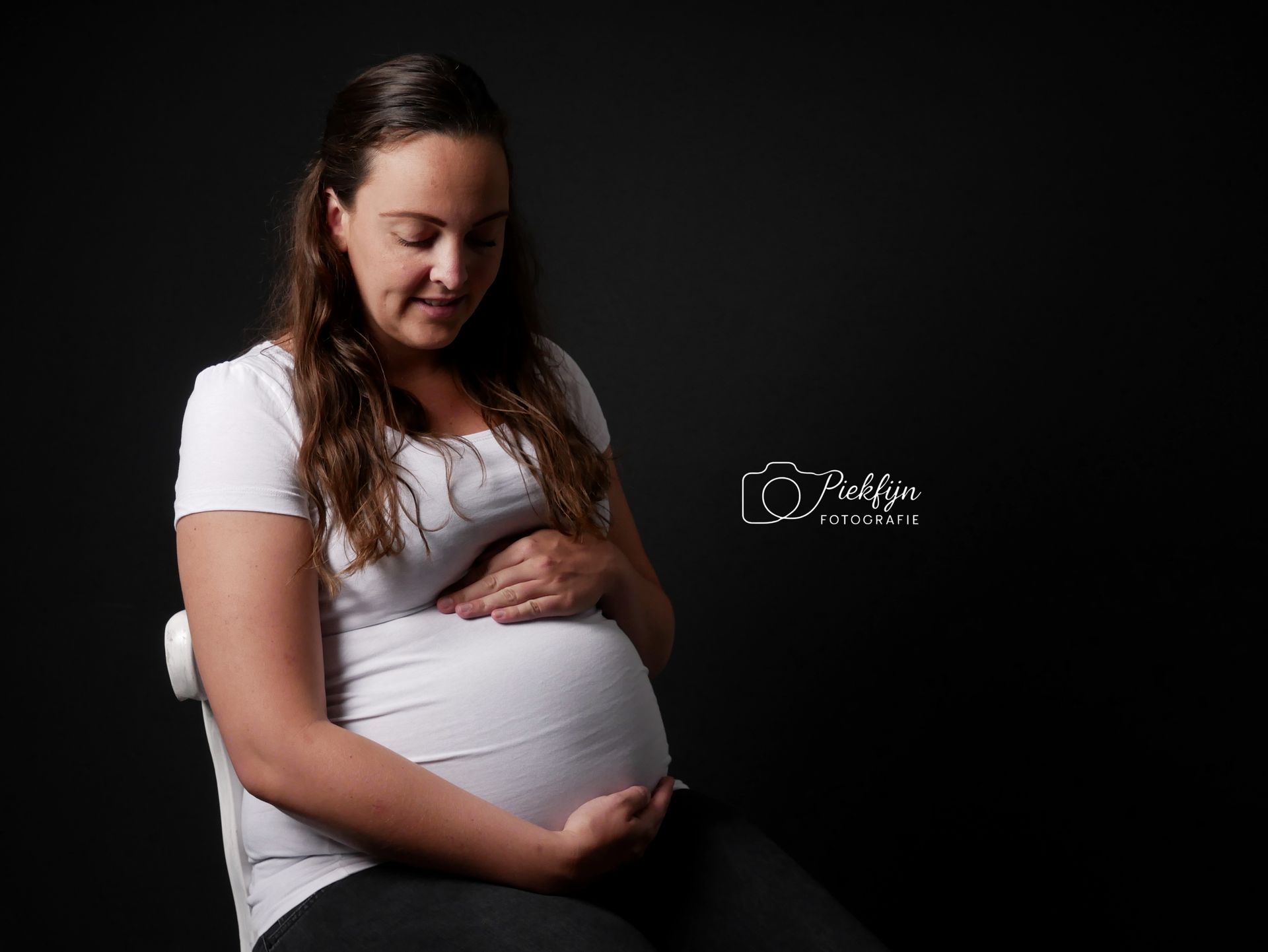 Een zwangere vrouw zit op een stoel en houdt haar buik vast.