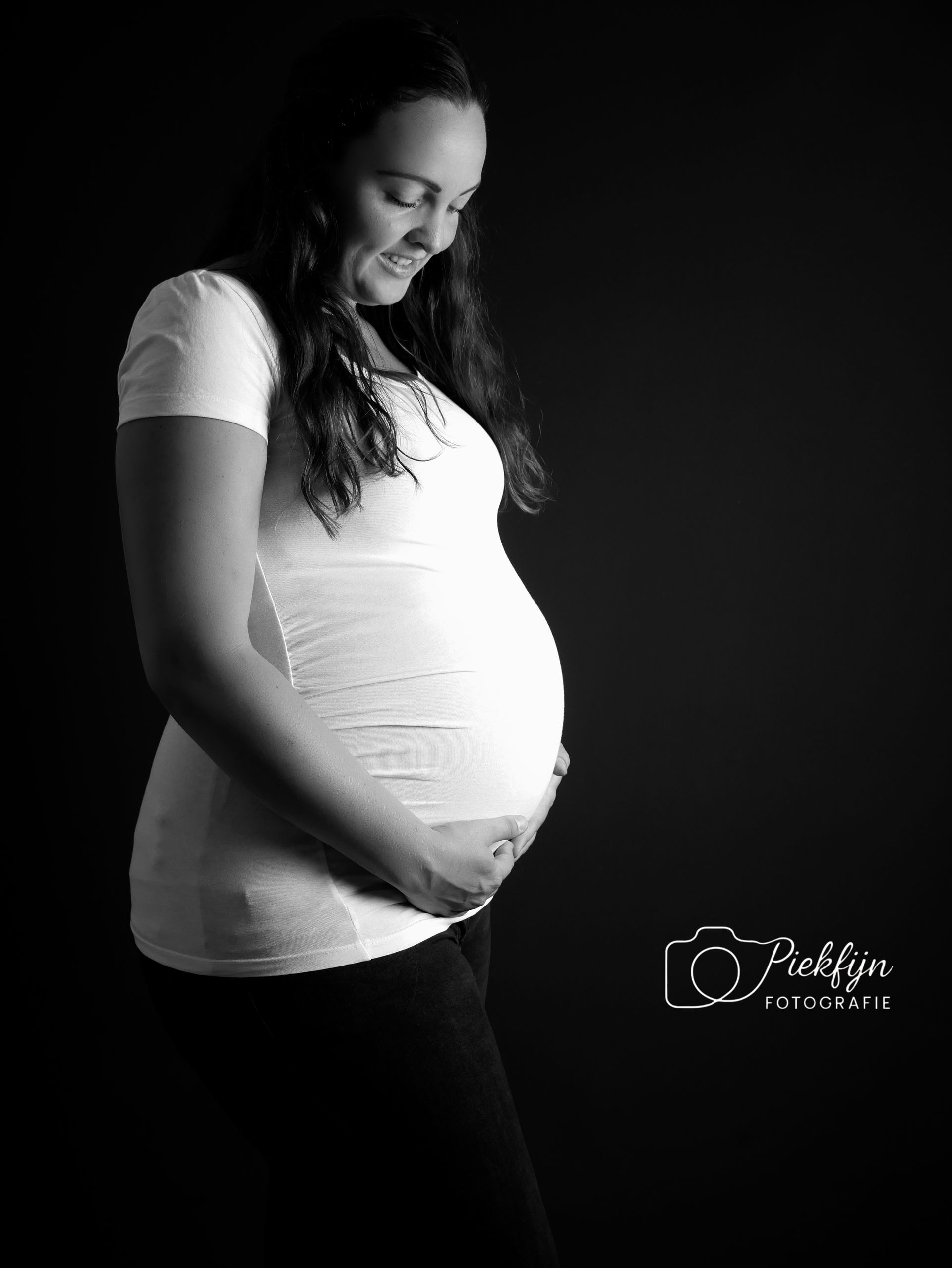 Een zwart-witfoto van een zwangere vrouw die haar buik vasthoudt.