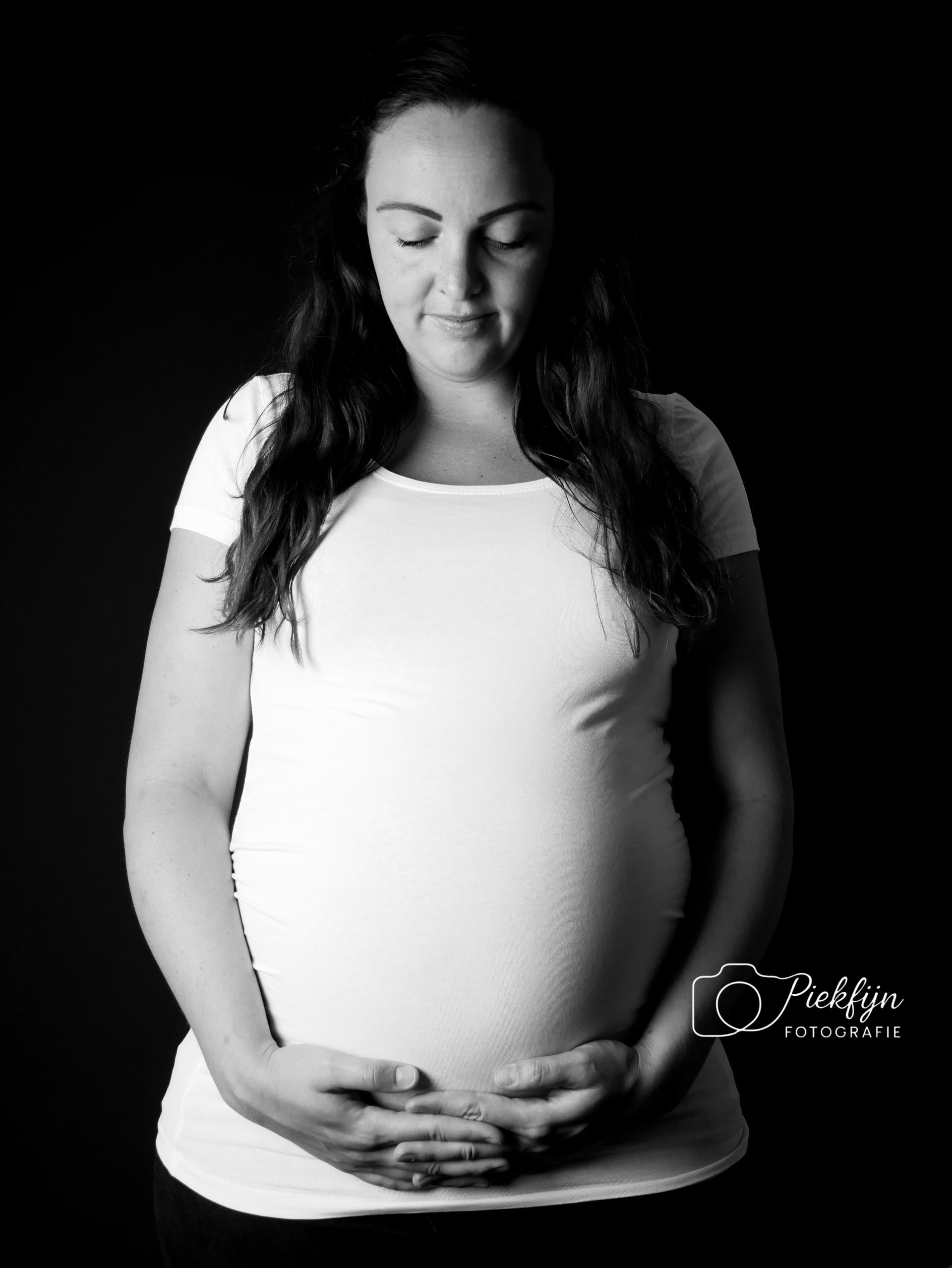 Een zwangere vrouw houdt haar buik vast op een zwart-witfoto.