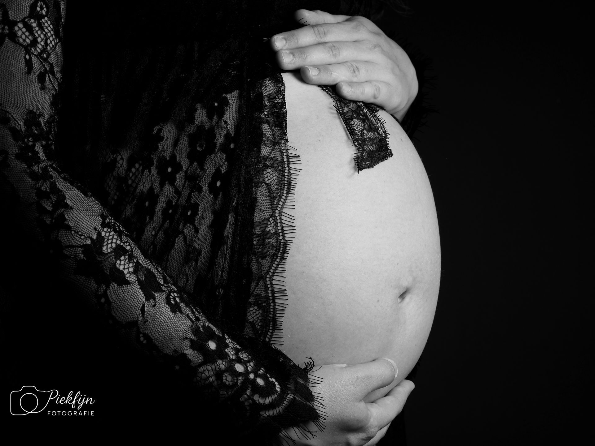 Een zwart-witfoto van een zwangere vrouw die haar buik vasthoudt.