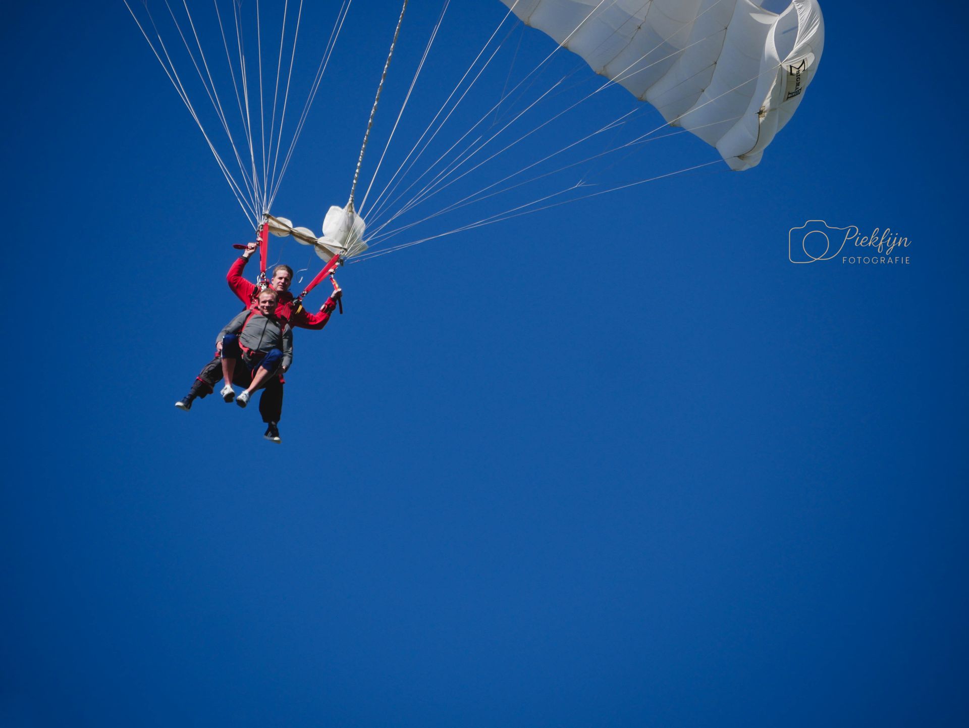 Een persoon vliegt door de lucht met een witte parachute