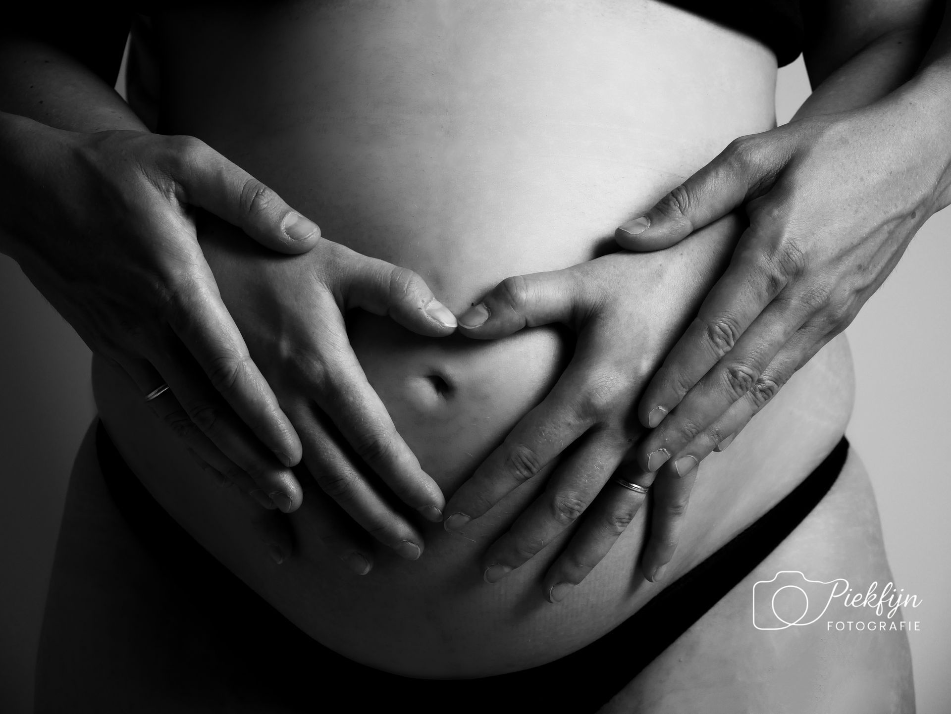 Een zwangere vrouw maakt een hartvorm met haar handen op haar buik.