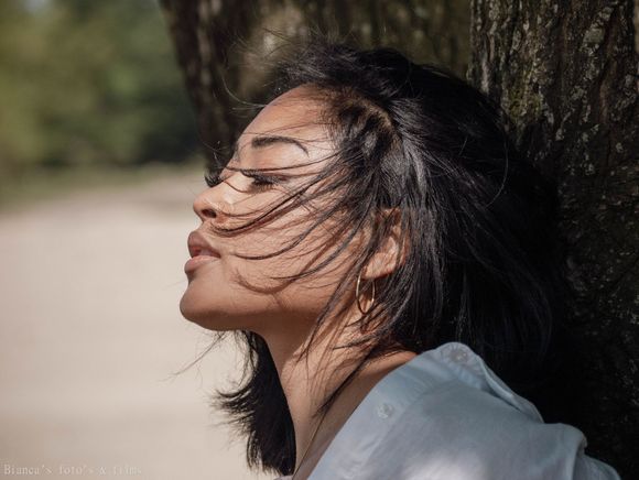 Een vrouw leunt tegen een boom, met haar haar wapperend in de wind.