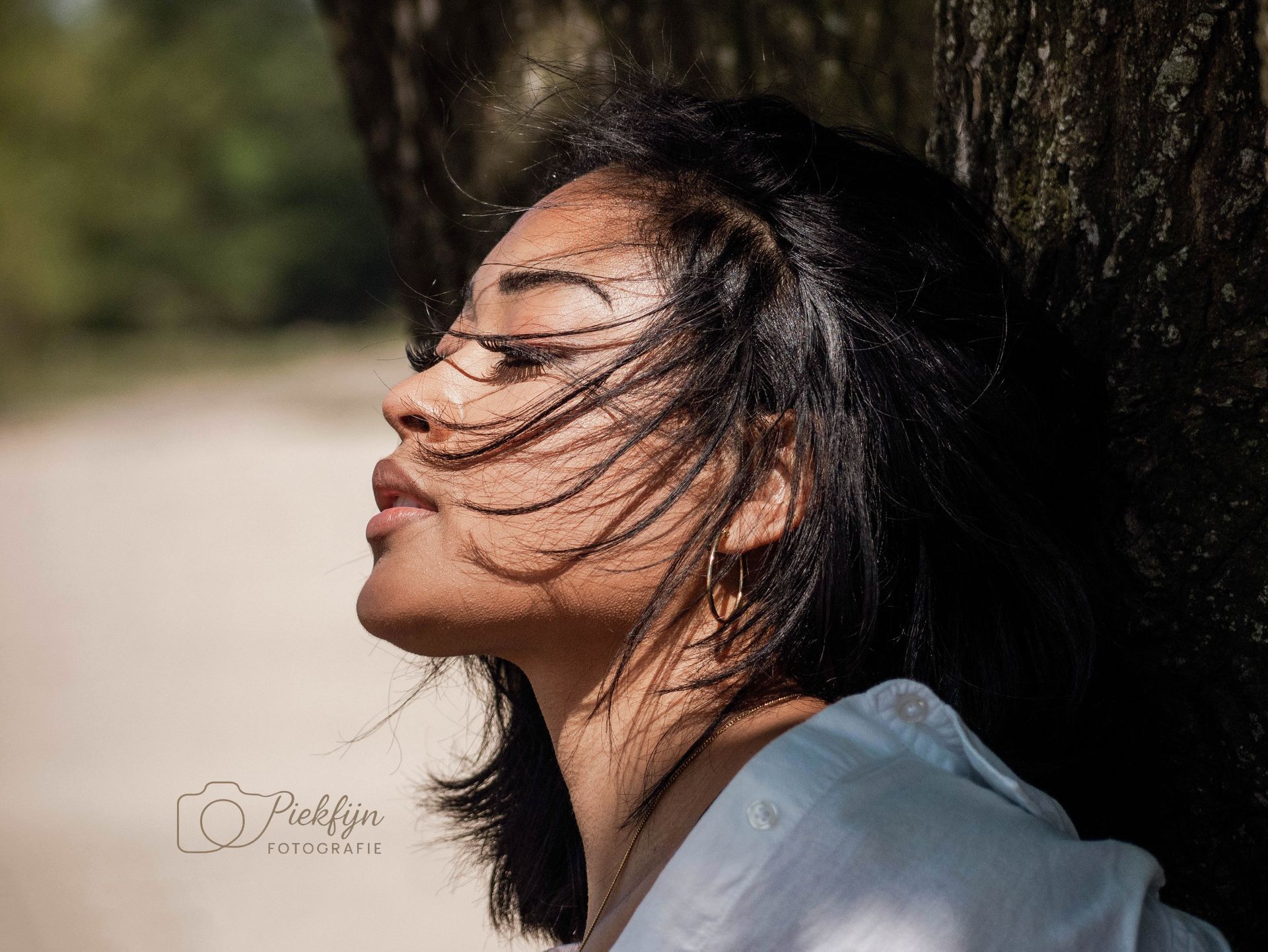 Een vrouw leunt tegen een boom, met haar haar wapperend in de wind.
