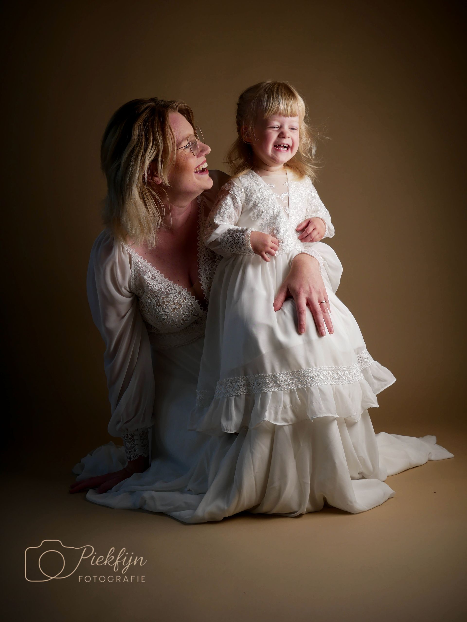 Een vrouw knielt naast een klein meisje in een witte jurk.