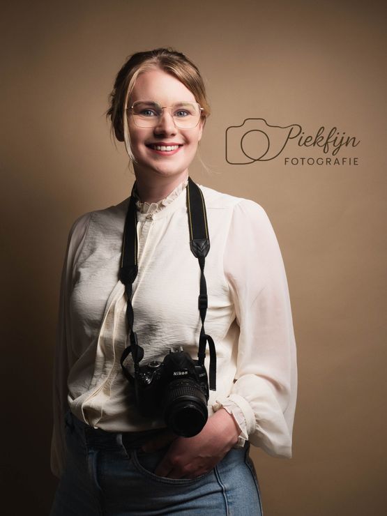 Een vrouw houdt een camera om haar nek en lacht.