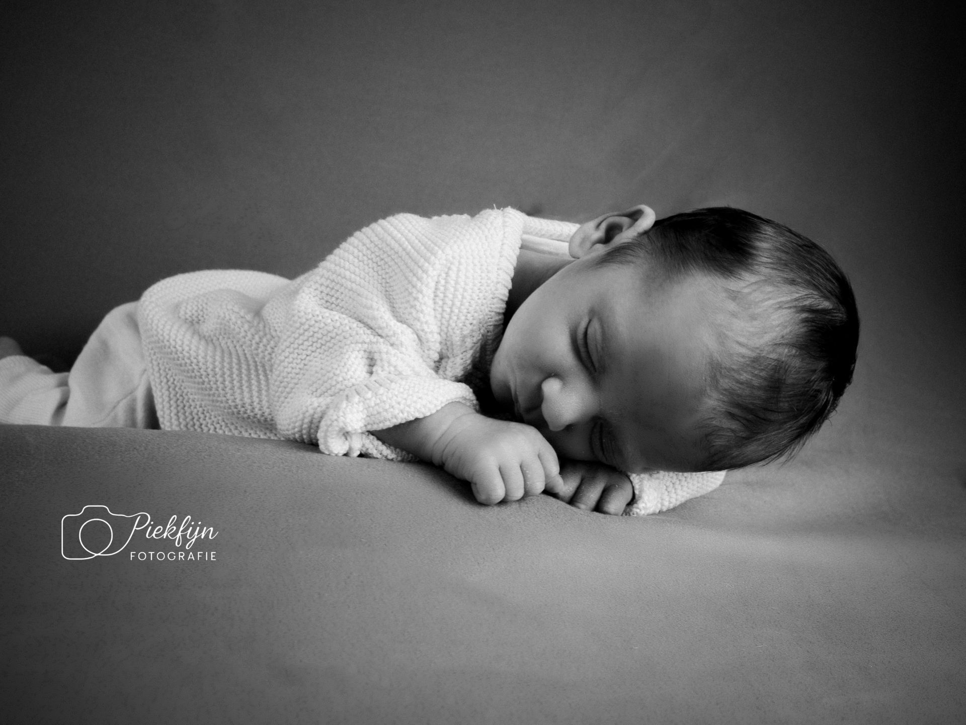 Een zwart-witfoto van een pasgeboren baby die op een bed slaapt.
