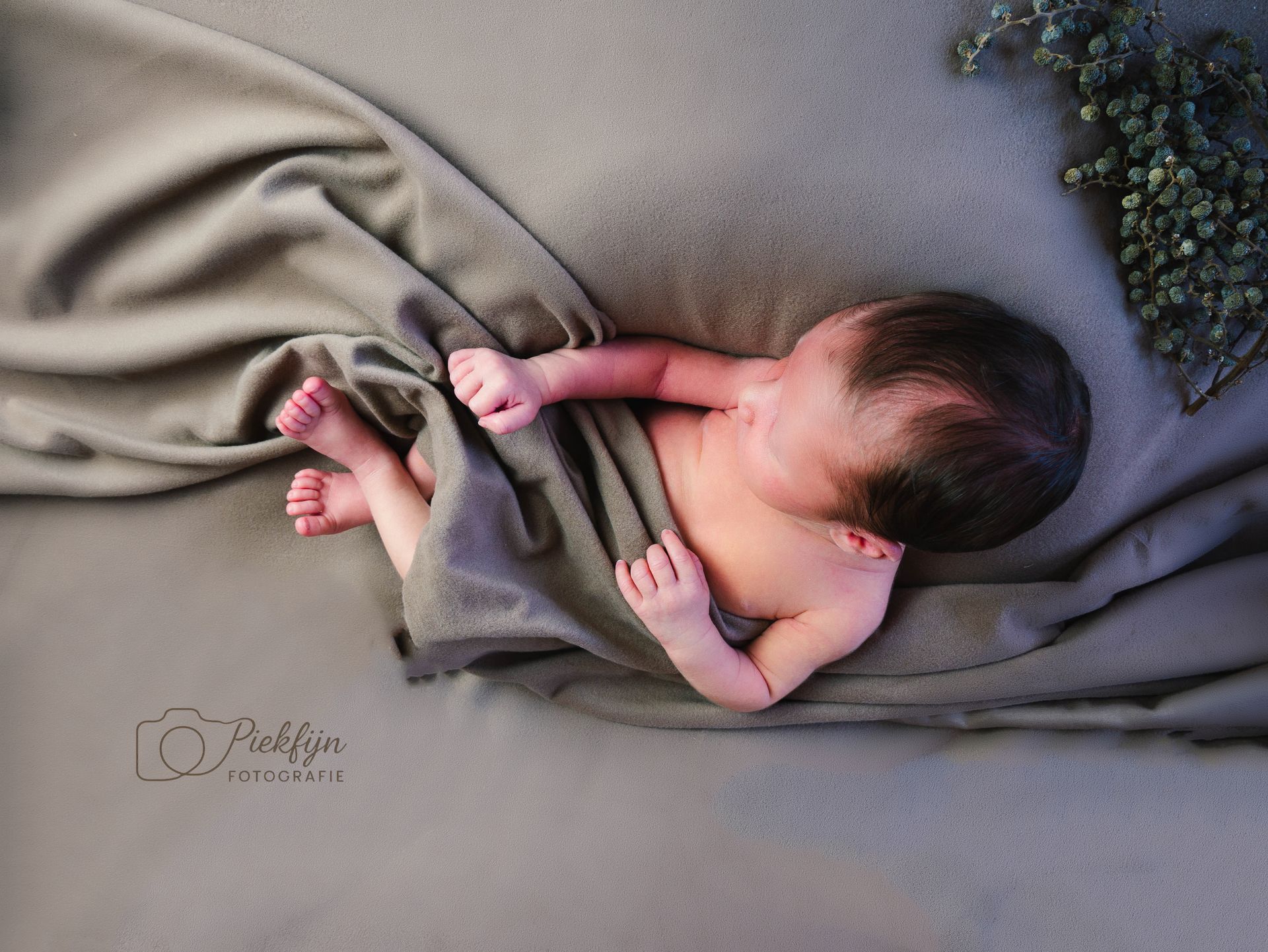 Een pasgeboren baby, gewikkeld in een deken, slaapt op een bed.