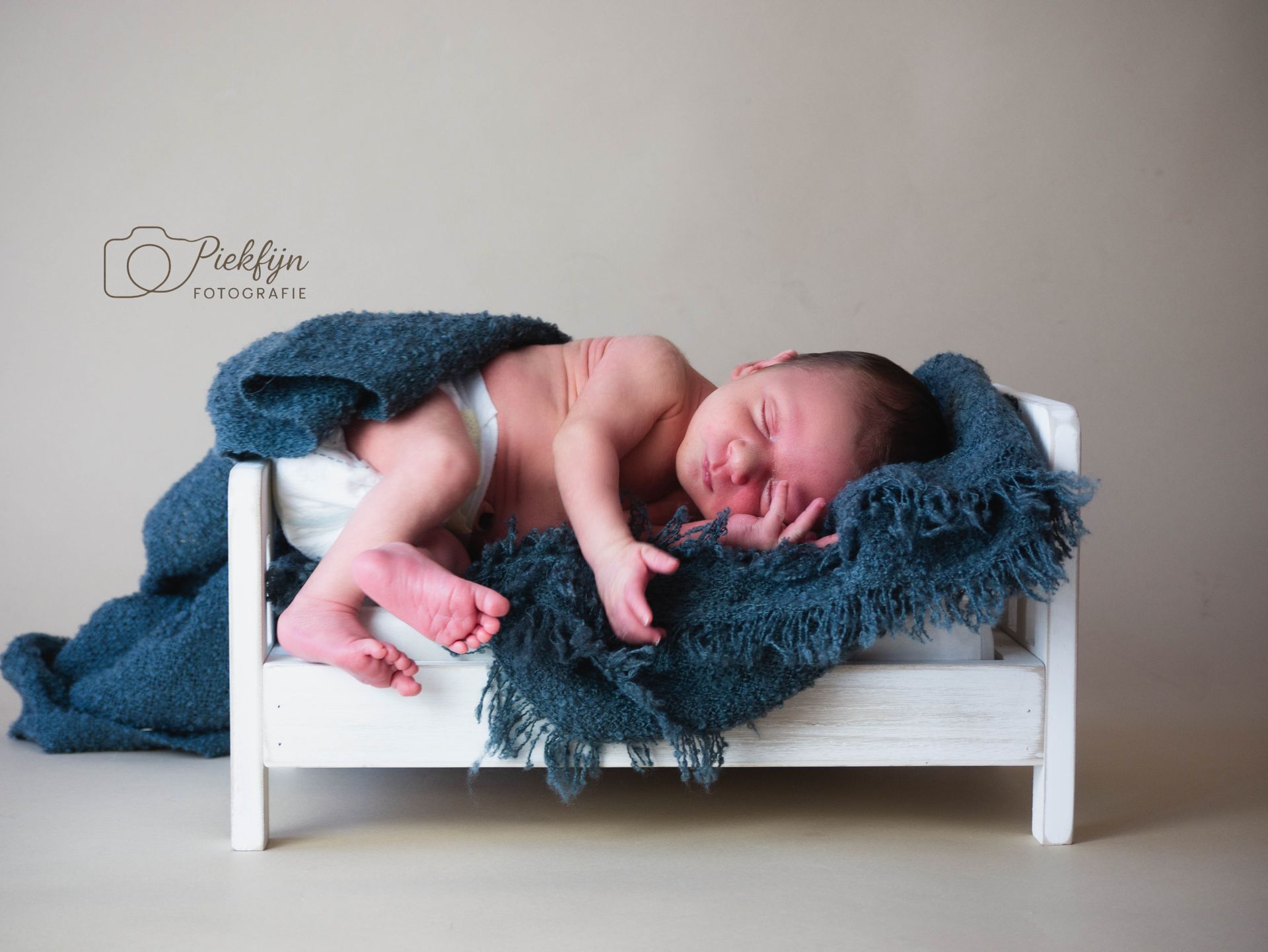 Een pasgeboren baby slaapt in een klein bedje met een blauwe deken.