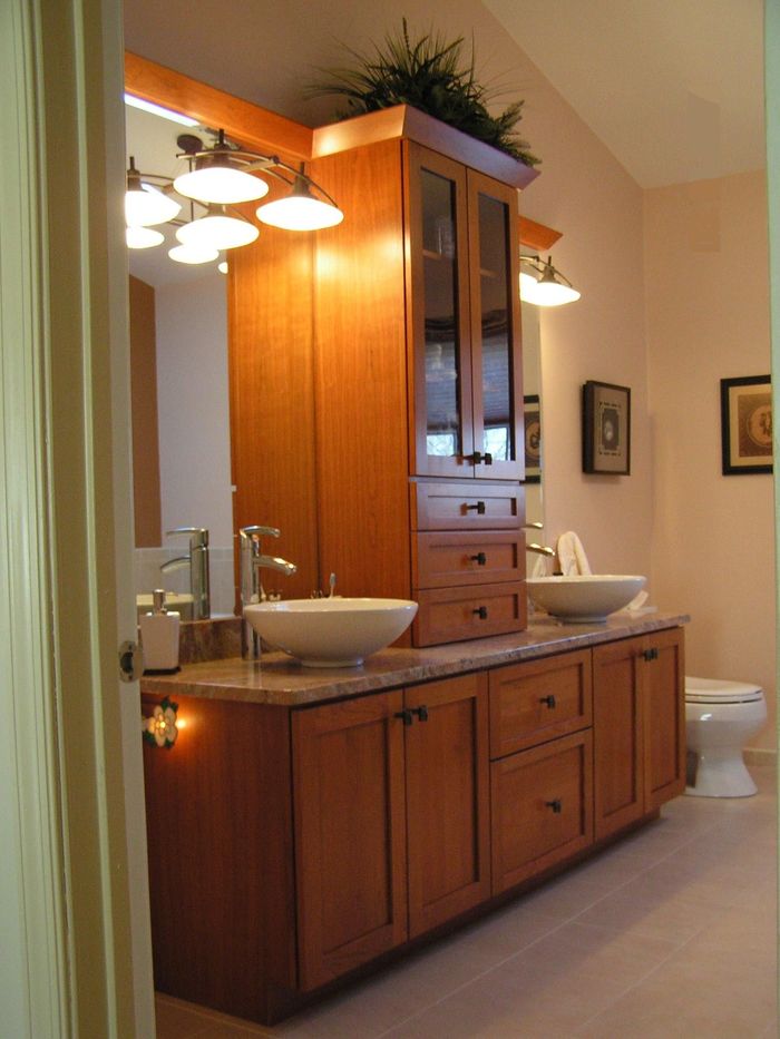 Bathroom vanity with two vessel sinks, wood cabinets, and overhead lighting.
