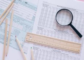 A magnifying glass is sitting on top of a piece of paper next to a ruler and pencils.