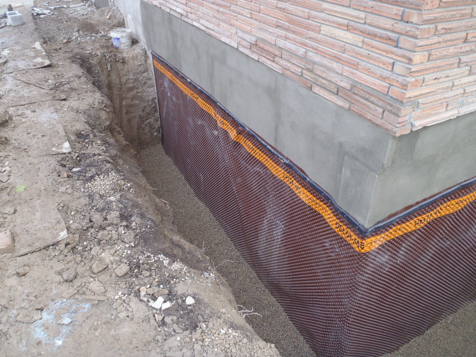 Foundation wall with brown drainage membrane, trench, and brick.