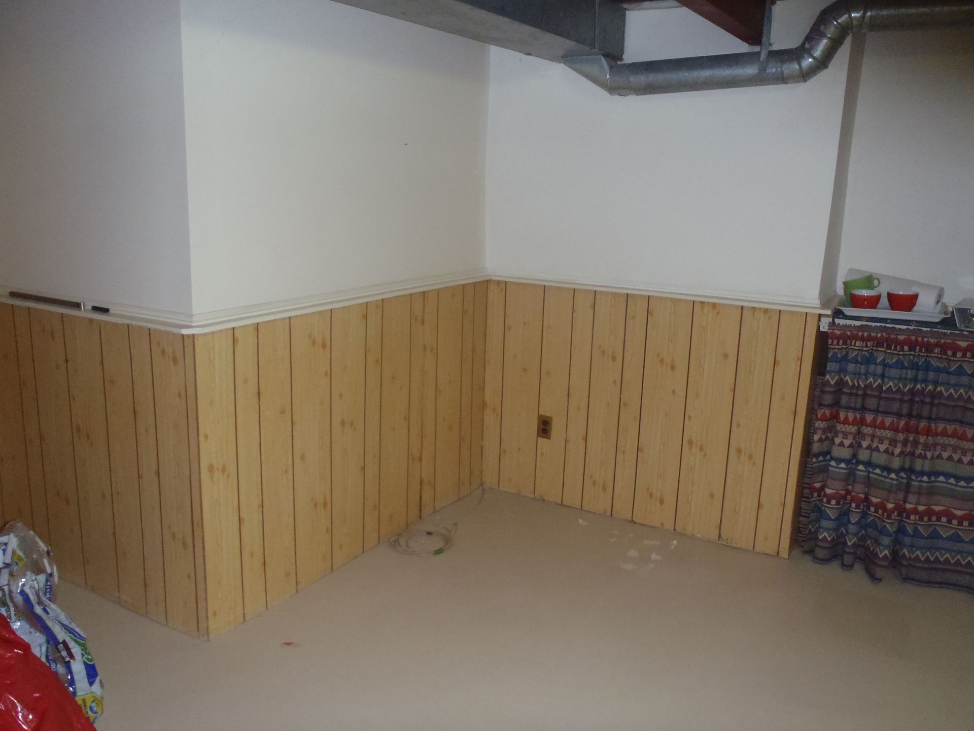 Wooden paneling on walls in a beige room corner; white painted upper walls, exposed ductwork, and floor.