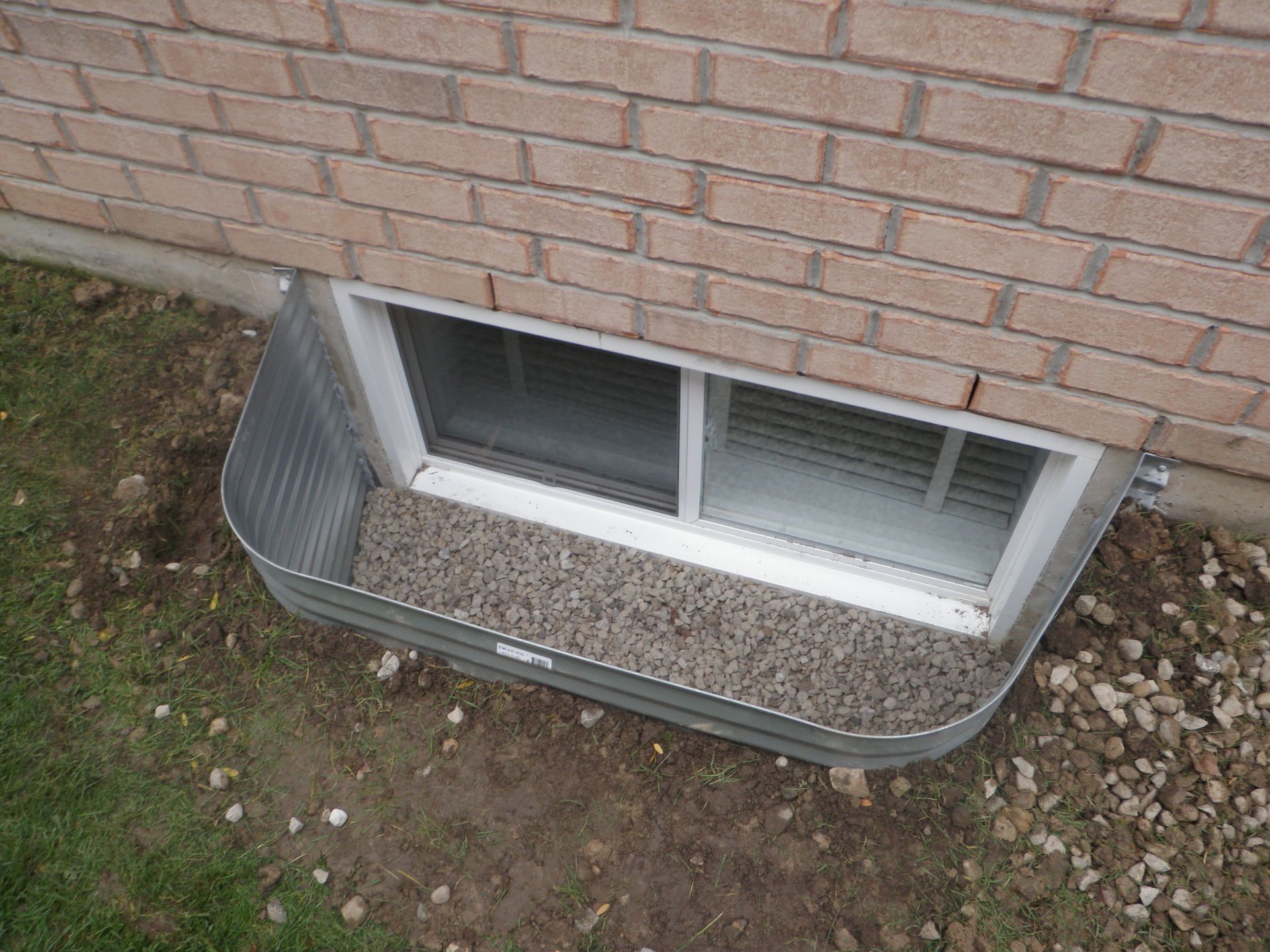 A window in the basement of a brick house.