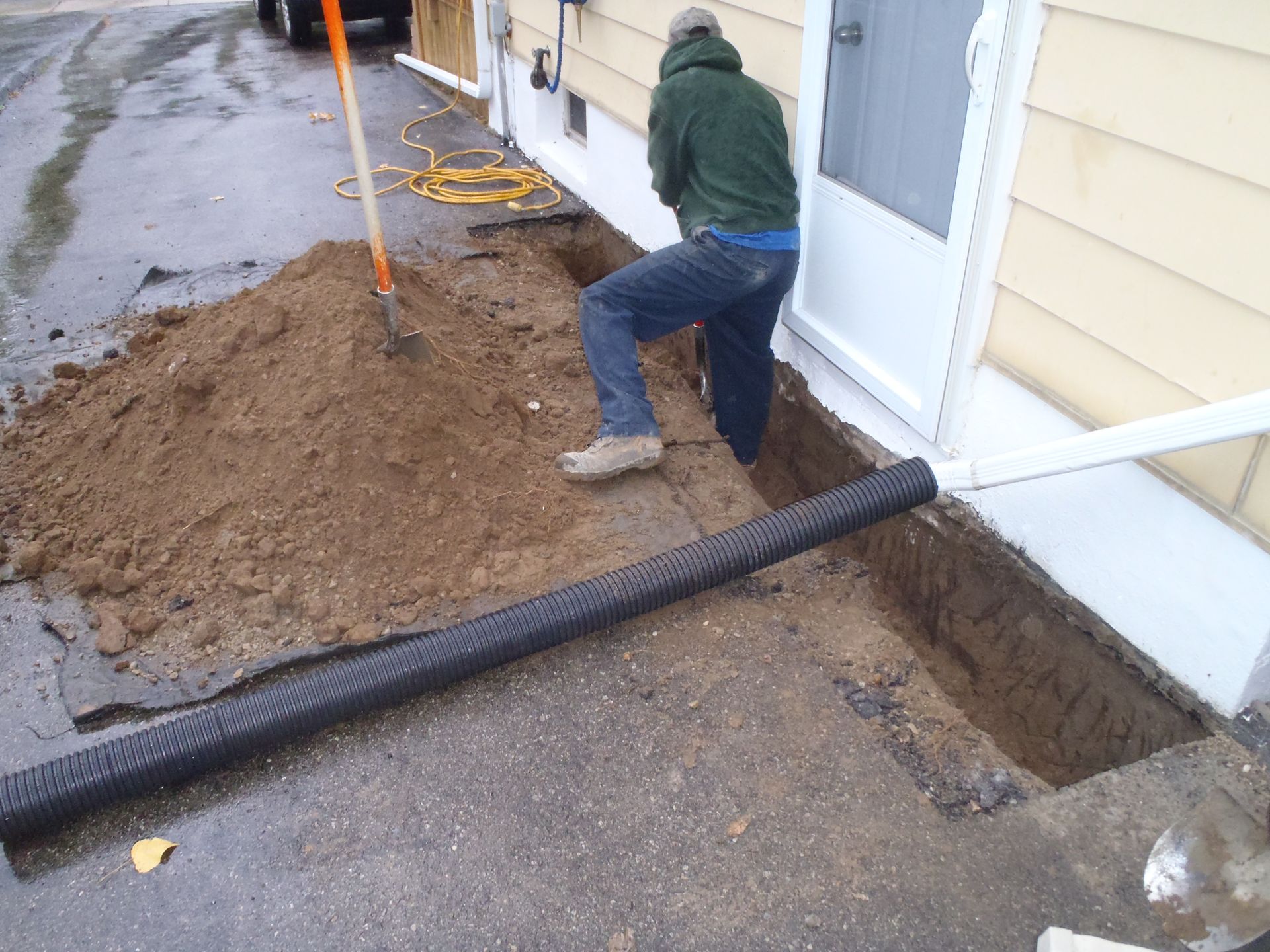 Person digging a trench next to house foundation.