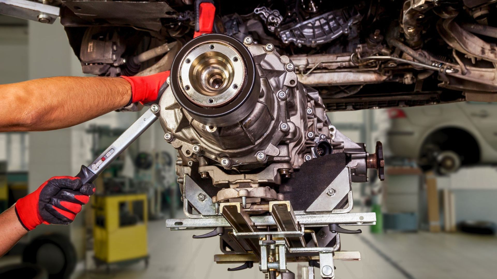 Mechanic working on car's undercarriage with tools in a repair shop. Transmission on a support.