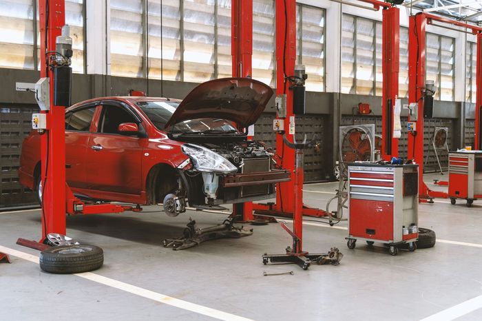 Red car on a lift in a garage, hood open. Several red lifts and toolboxes are visible.