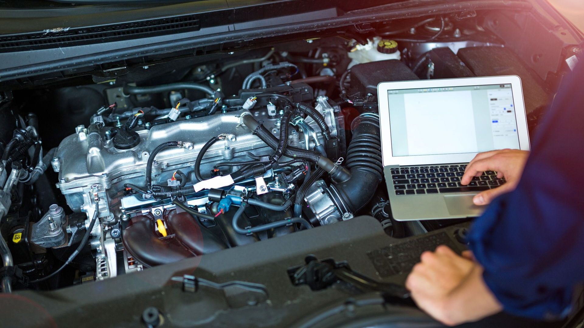 Mechanic using a laptop to diagnose a car engine in a garage.
